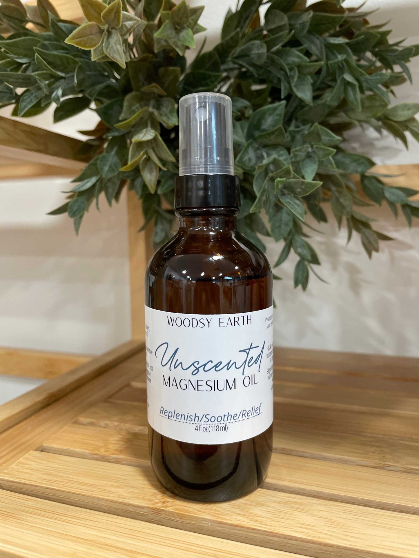 Bottle of Woodsy Earth Unscented Magnesium Oil Spray in a 4oz amber glass bottle with spray top, placed on a wooden surface with green plant background