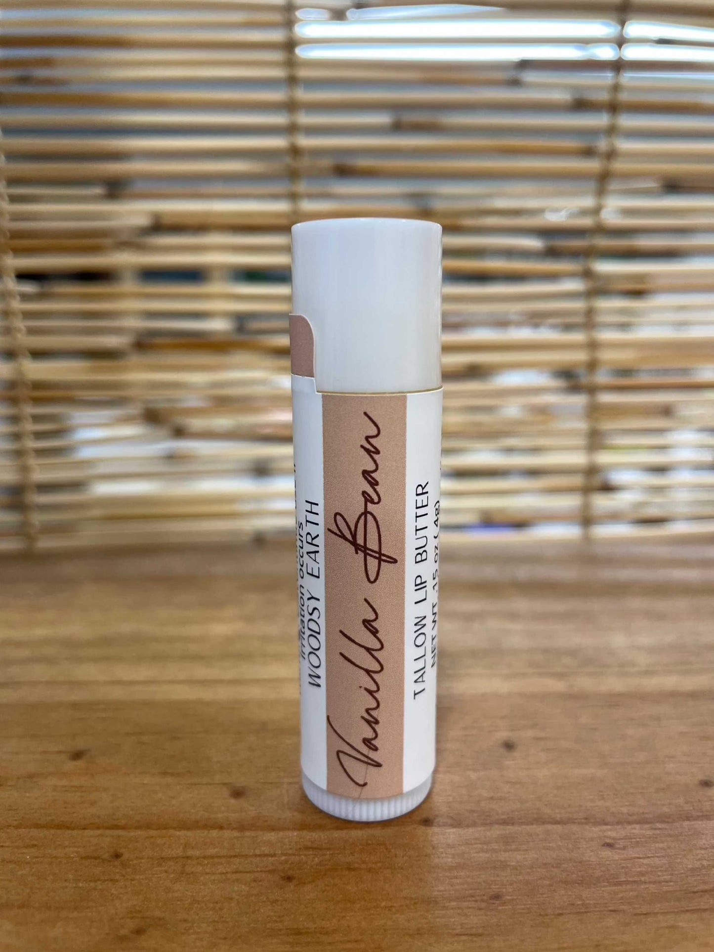 Woodsy Earth Vanilla Bean Tallow Lip Butter tube on a wooden surface with bamboo background
