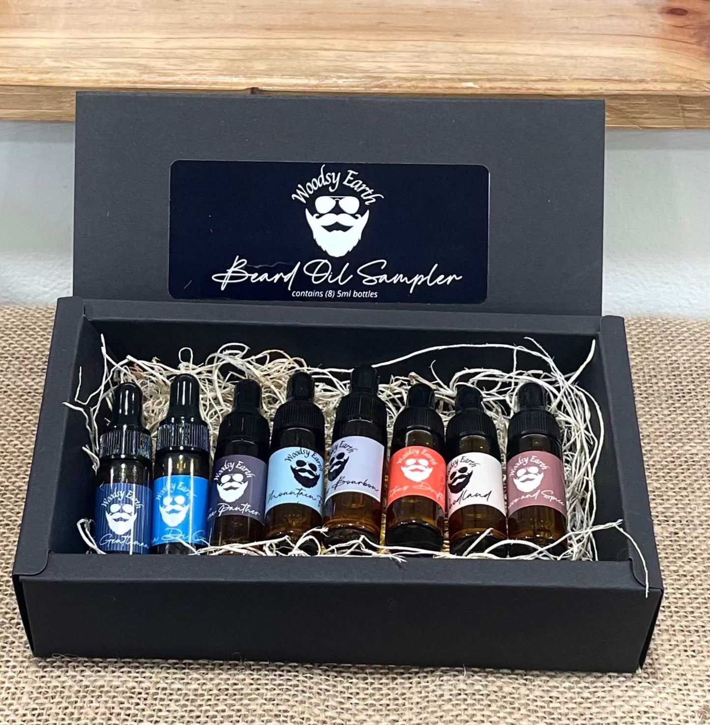 Woodsy Earth Beard Oil Sampler Gift Set with eight 5ml dropper bottles in a black box. Includes multiple natural scents for beard grooming and care.