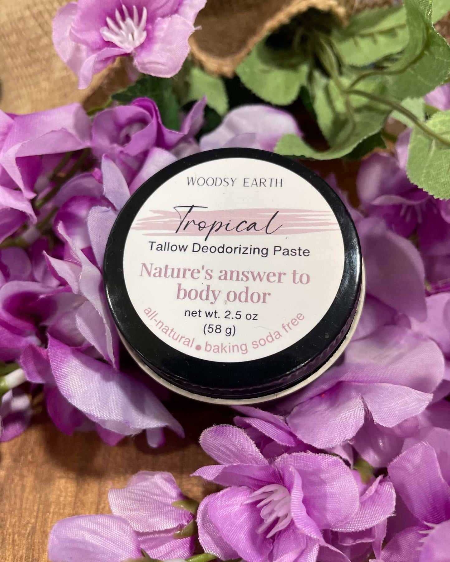 Woodsy Earth Tropical Tallow Deodorant Paste in 2.5 oz jar surrounded by purple flowers, natural baking soda free formula