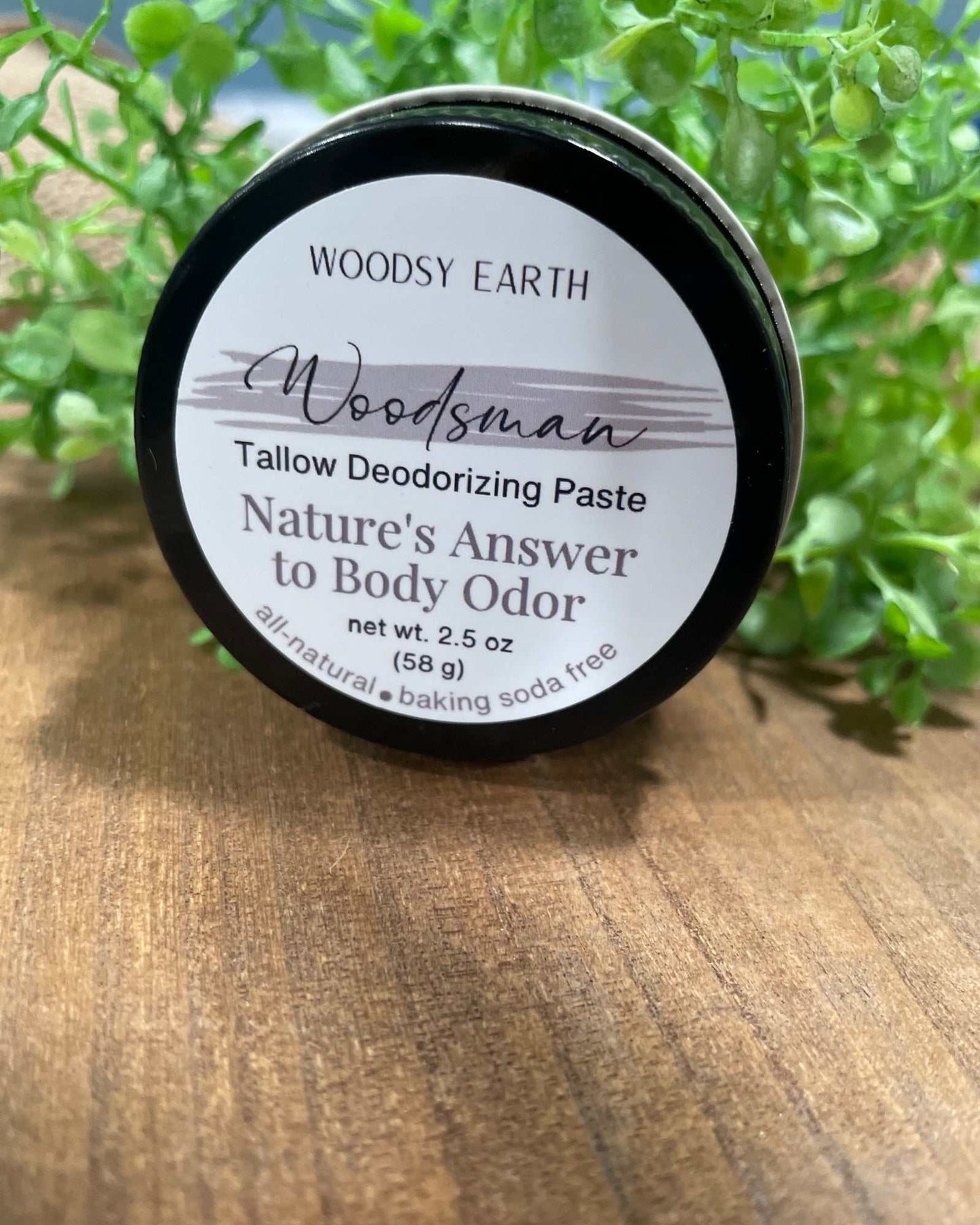 Woodsy Earth Woodsman Tallow Deodorant Paste in 2.5 oz jar on wooden surface with greenery background, natural baking soda free formula