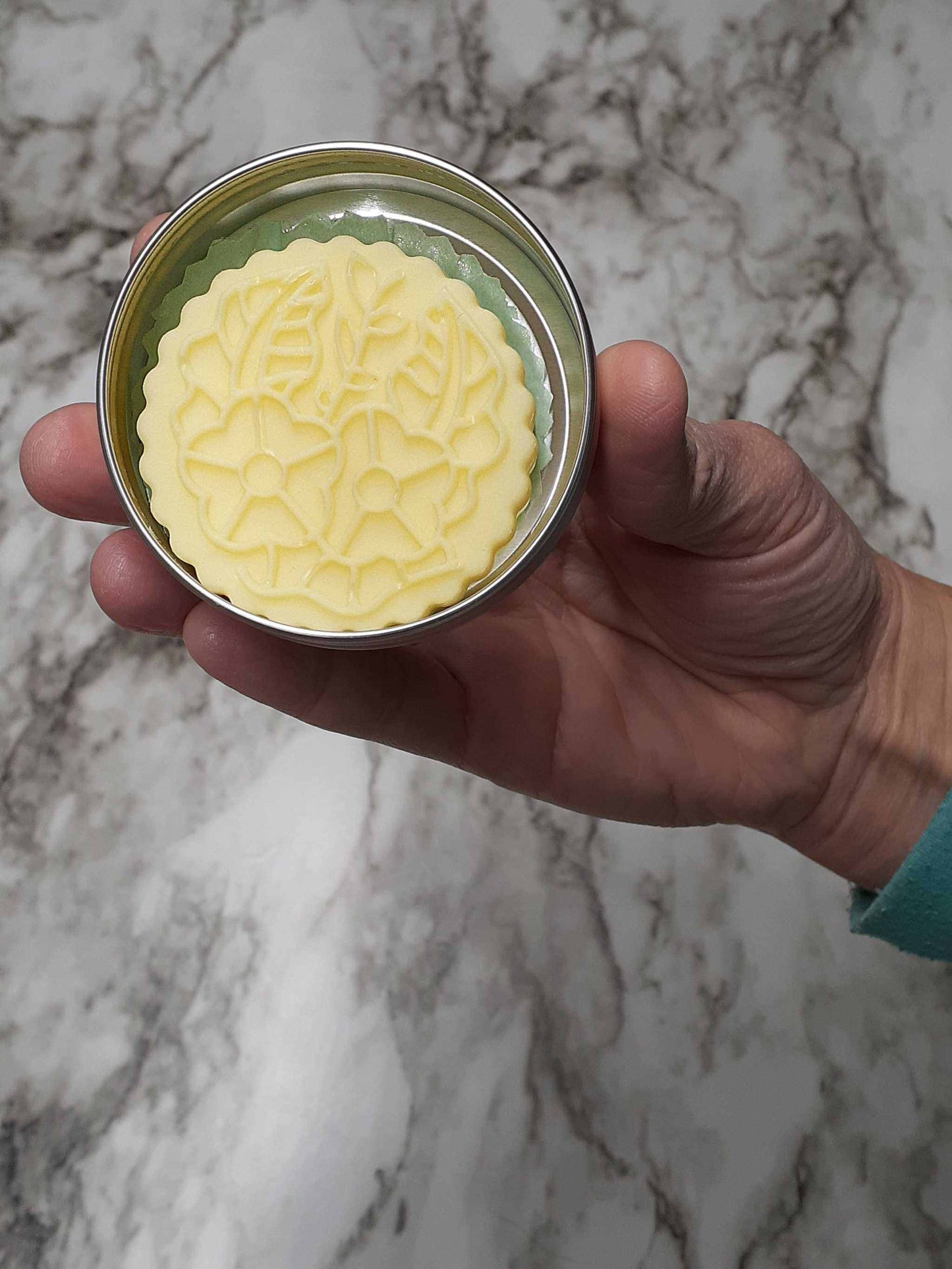 Eucalyptus Mint Tallow Lotion Bar in decorative tin, hand-held, offering refreshing scent and moisturizing benefits.