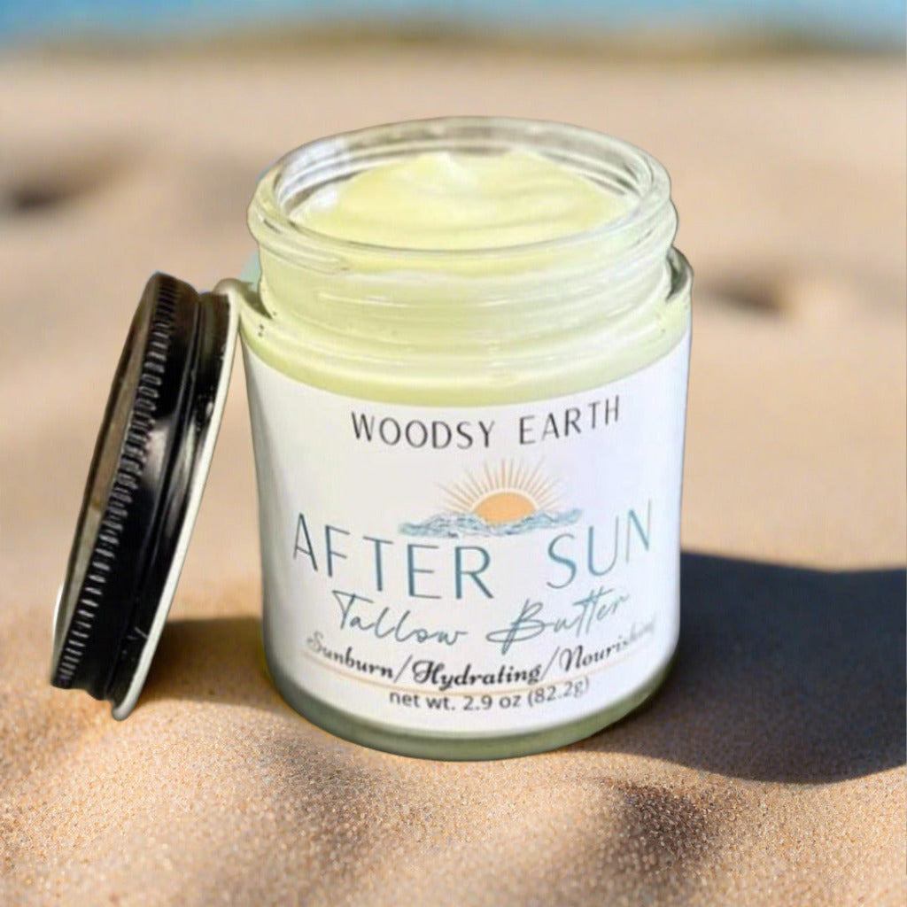 Open jar of Woodsy Earth After Sun Tallow Butter on sand, natural soothing moisturizer for sunburn relief, hydration, and nourishing skin care