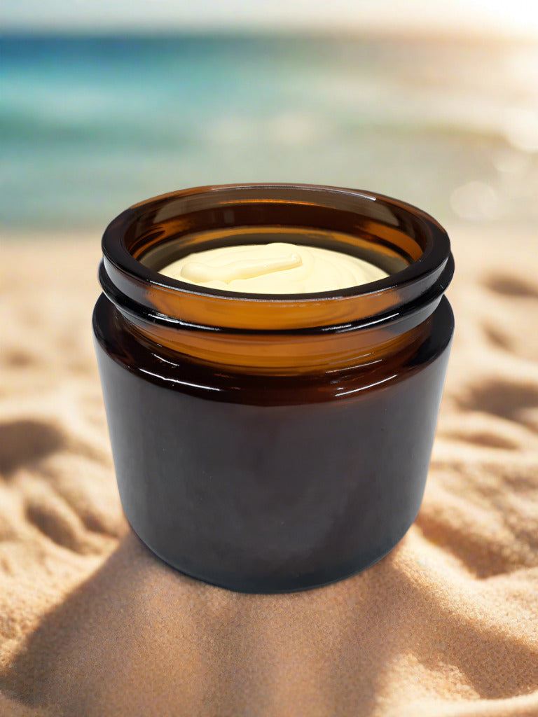 Open amber jar of Woodsy Earth Before Sun Tallow Butter on sandy beach, natural non-toxic sunscreen with zinc oxide for skin protection and hydration