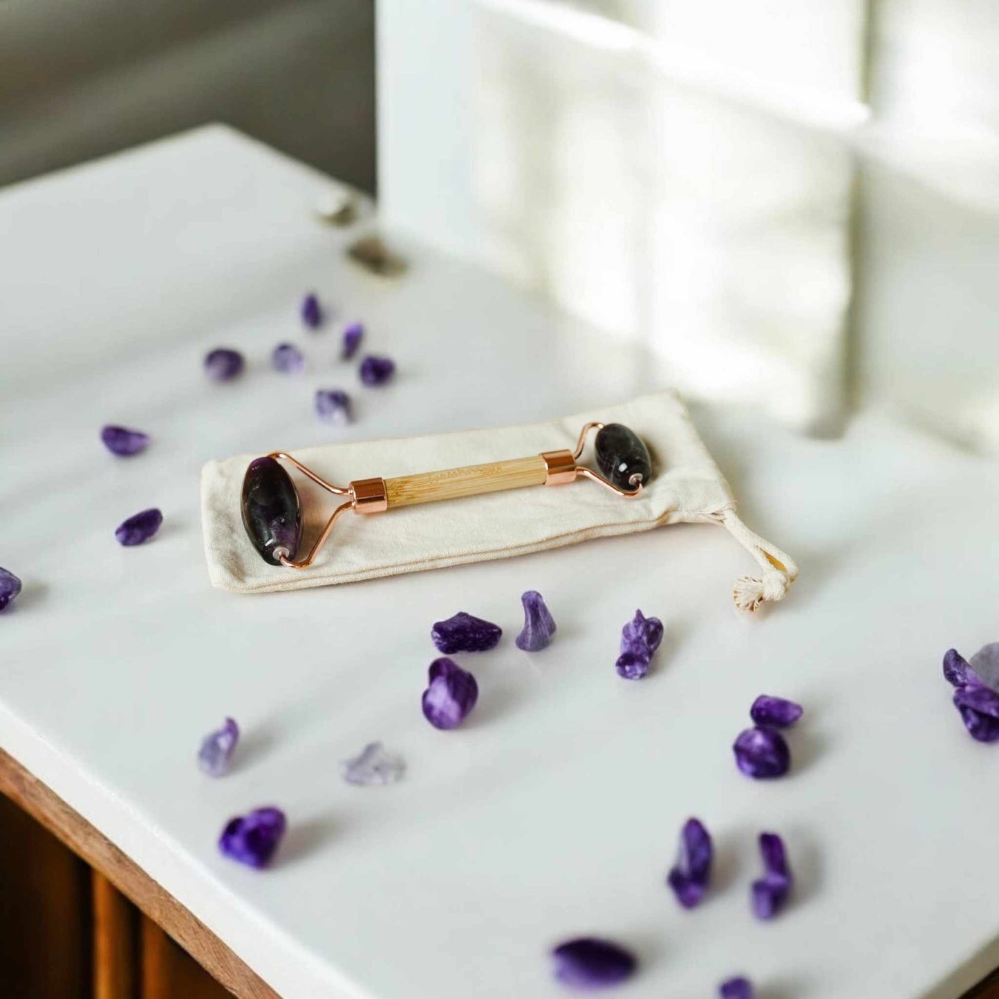 Bamboo Switch bamboo facial massage roller with rose quartz stone on a white surface surrounded by purple crystals.