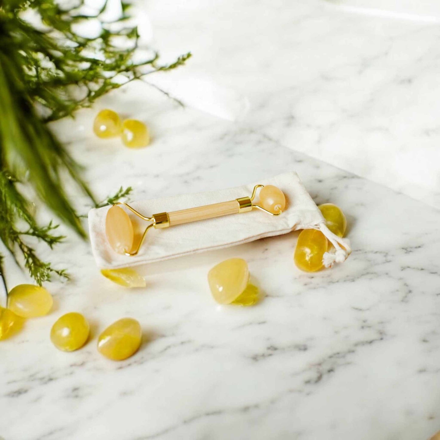 Bamboo Switch bamboo facial massage roller with rose quartz on a marble surface surrounded by stones.