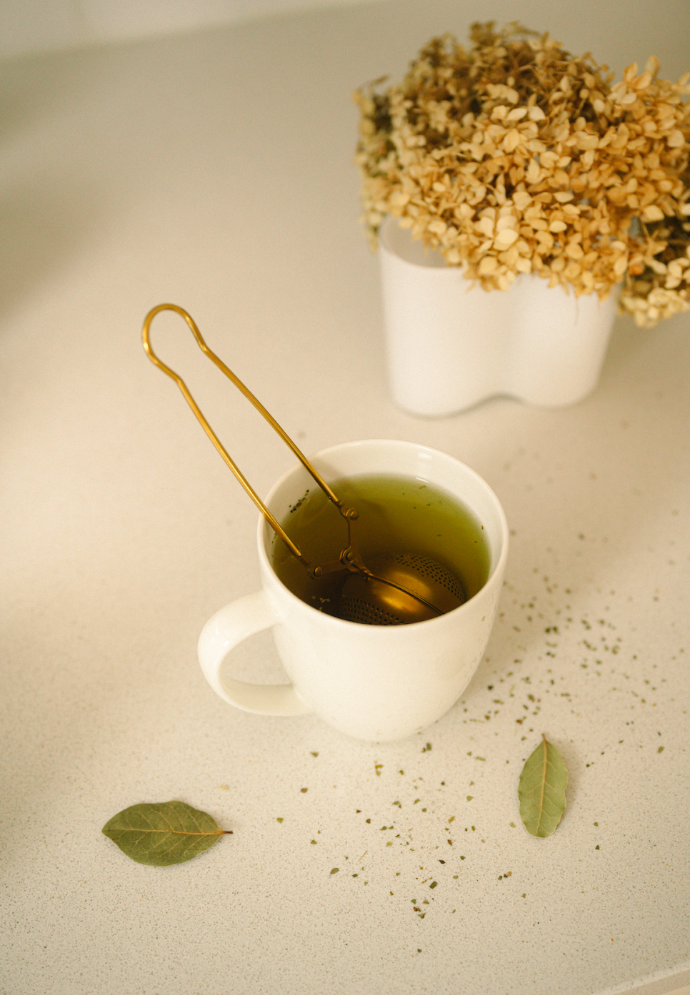 Bamboo Switch gold stainless steel tea strainer steeping loose leaf tea in a white mug on a countertop.