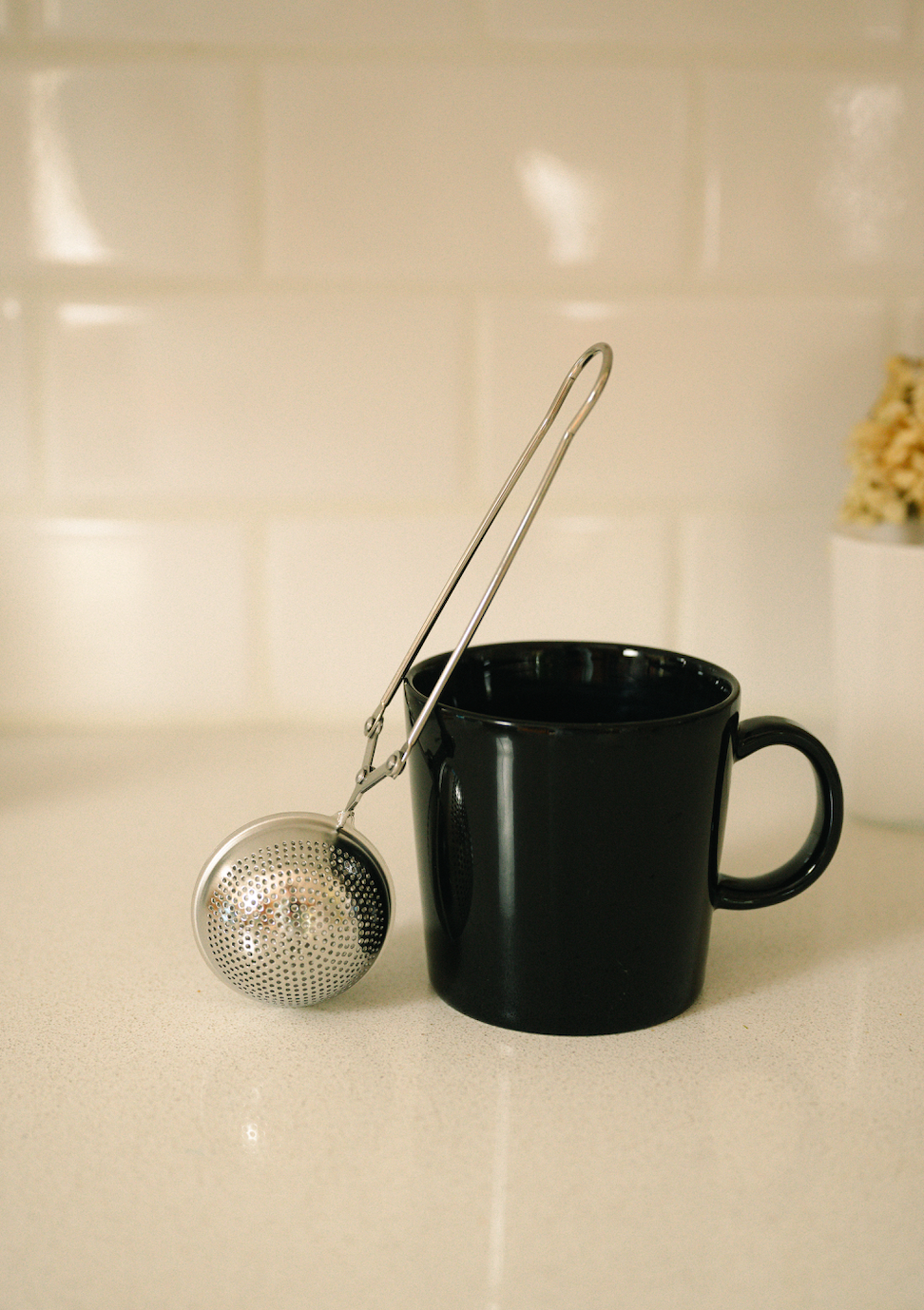 Bamboo Switch stainless steel tea strainer resting against a black mug on a light countertop.