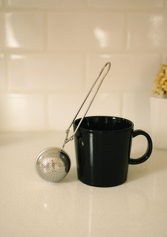 Bamboo Switch stainless steel tea strainer resting against a black mug on a light countertop.