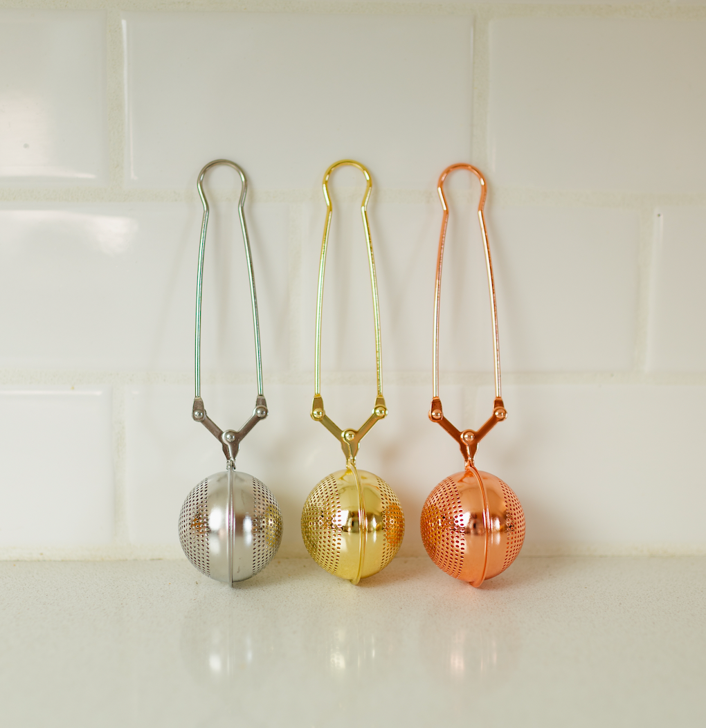 Bamboo Switch stainless steel tea strainers in silver, gold, and copper displayed against a white tile background.