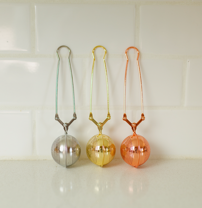 Bamboo Switch stainless steel tea strainers in silver, gold, and copper displayed against a white tile background.