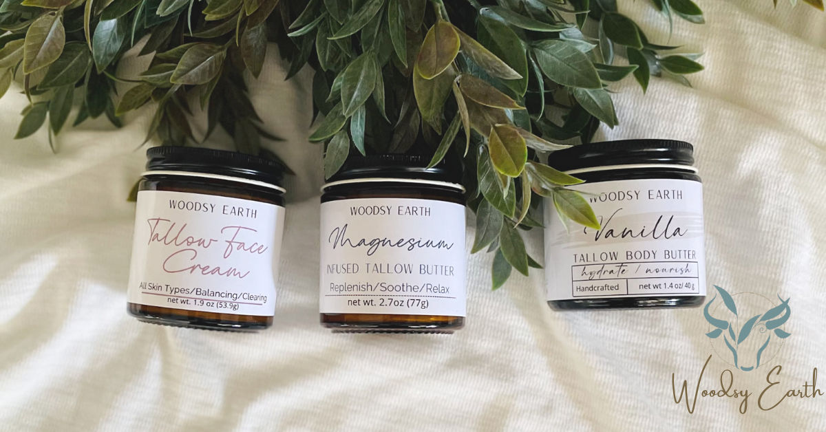 Woodsy Earth Tallow Face Cream, Magnesium Butter, and Vanilla Body Butter jars on white cloth with greenery, natural handcrafted skincare and wellness products.