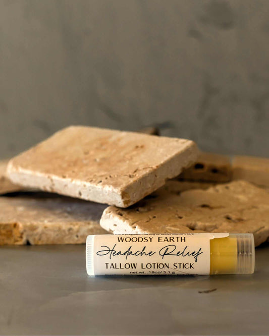 Woodsy Earth Headache Relief Tallow Lotion Stick in twist-up tube, natural pain relief balm made with essential oils, displayed on stone background.