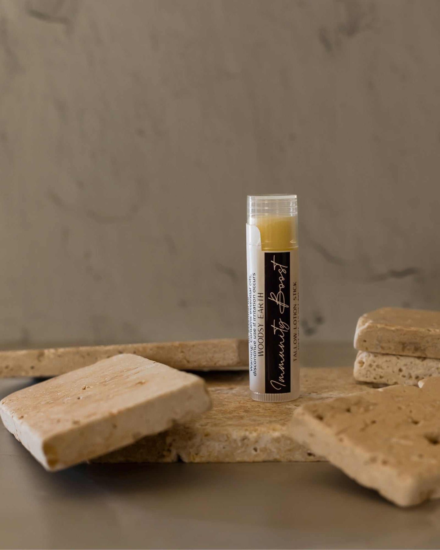 Woodsy Earth Immunity Boost Tallow Lotion Stick with essential oils for natural immune support, solid balm on stone background.