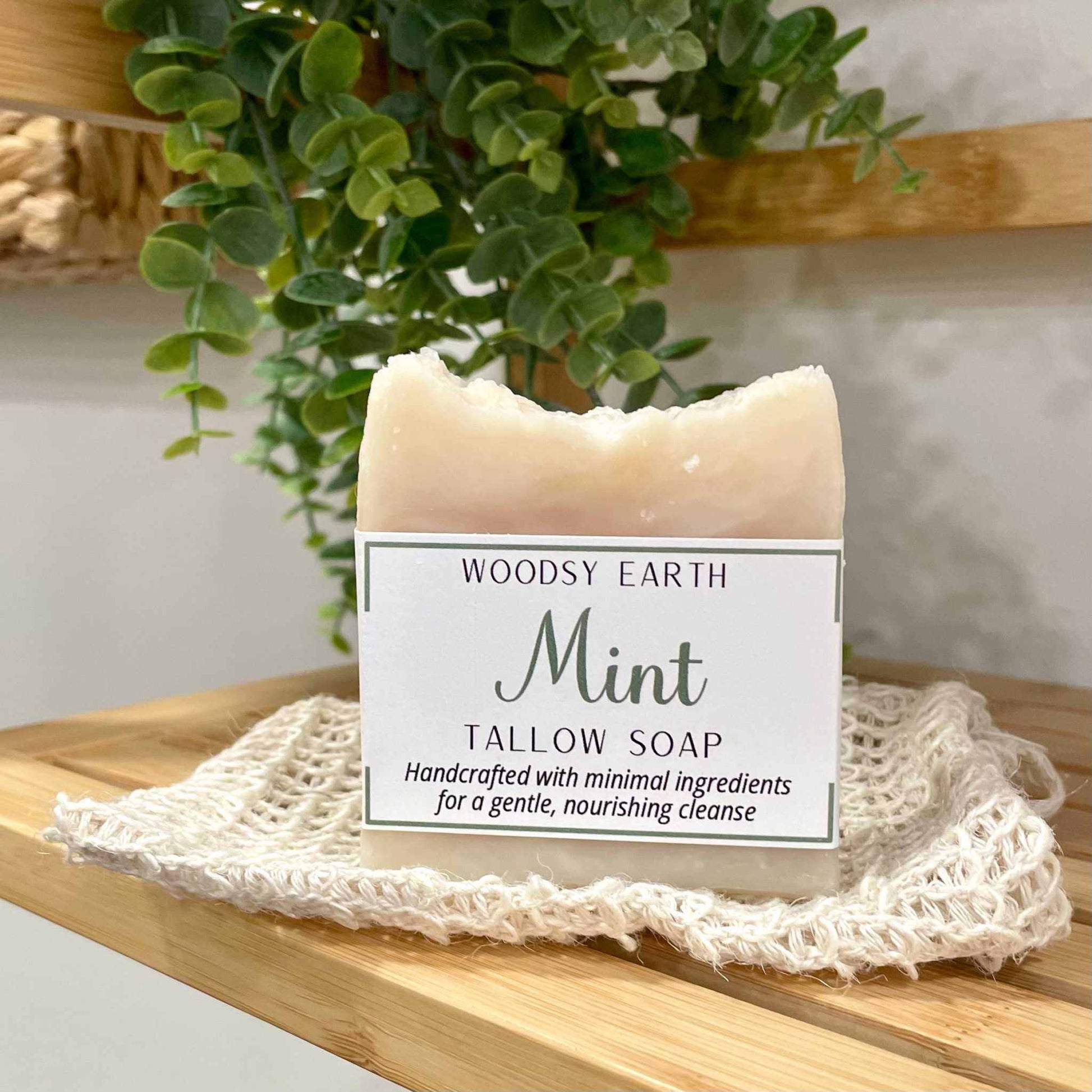 Bar of Woodsy Earth Mint Tallow Soap on a wooden surface with a plant in the background