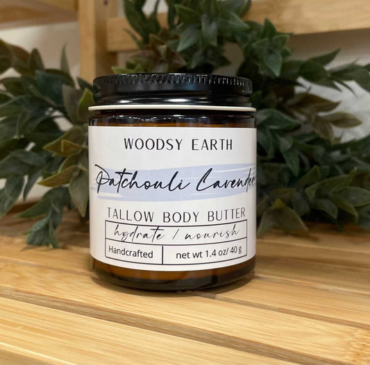 Woodsy Earth Patchouli Lavender Tallow Body Butter jar on wooden surface with green foliage, handcrafted natural moisturizer to hydrate and nourish skin