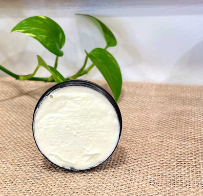Open 1 oz tin of Woodsy Earth Tallow Face Cream showing creamy texture, displayed on burlap with green plant in background