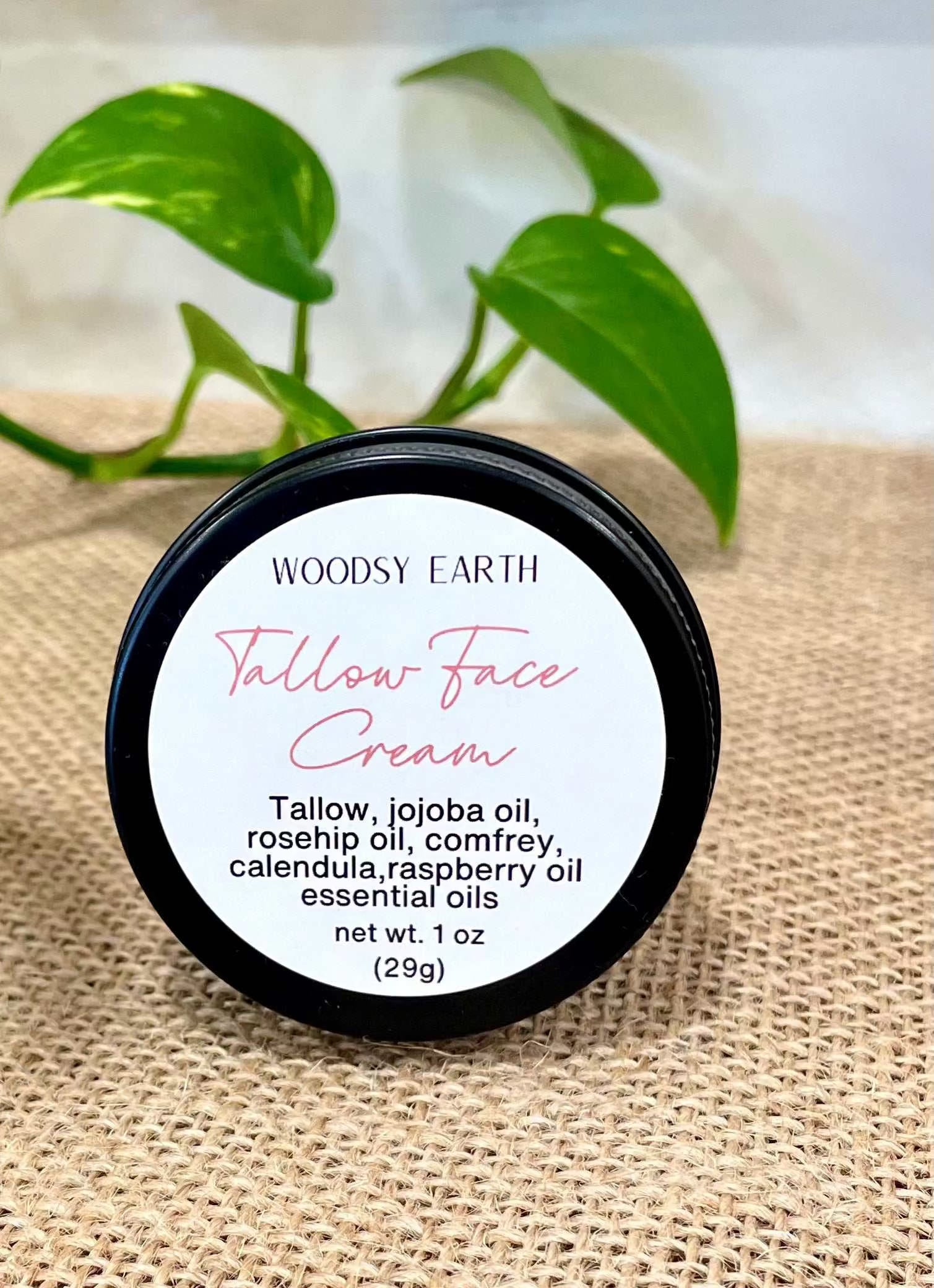 Woodsy Earth Tallow Face Cream, 1 oz travel tin with ingredients listed on label, displayed on burlap with green plant in background