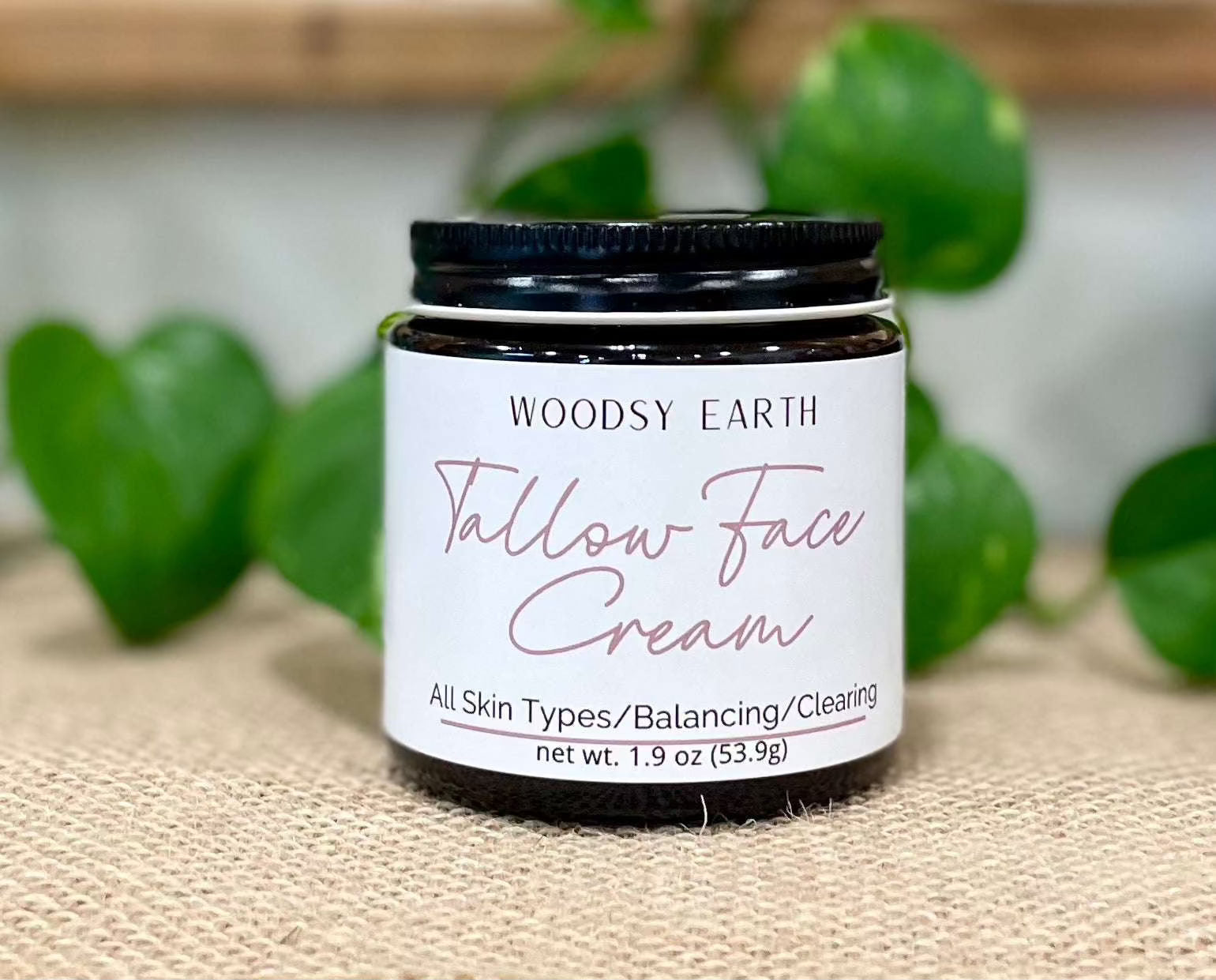 Woodsy Earth Tallow Face Cream jar for all skin types, balancing and clearing, displayed on burlap with greenery background