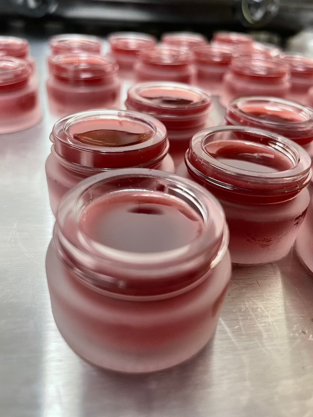 Batch of Woodsy Earth Tinted Tallow Lip Gloss in small glass jars, rich natural color and moisturizing formula.
