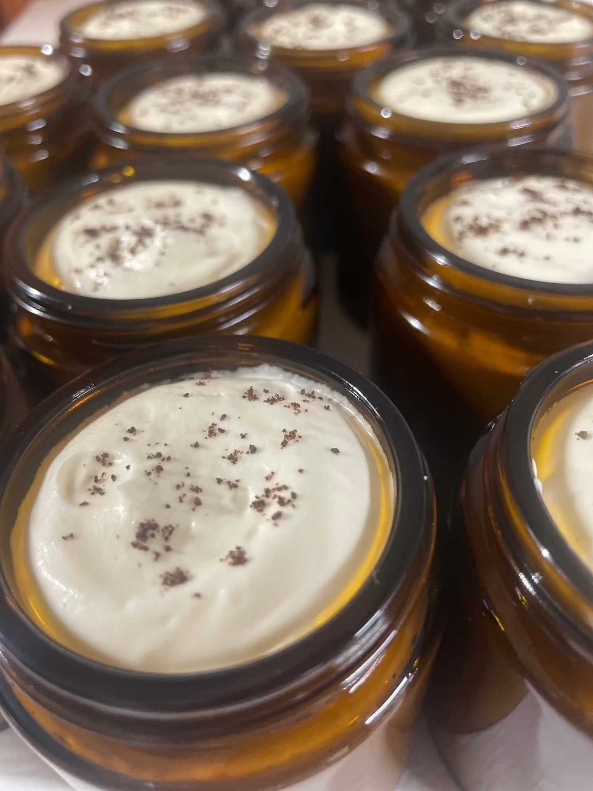 Whipped coffee body butter in amber jars, infused with tallow and topped with ground coffee for a creamy, moisturizing finish.